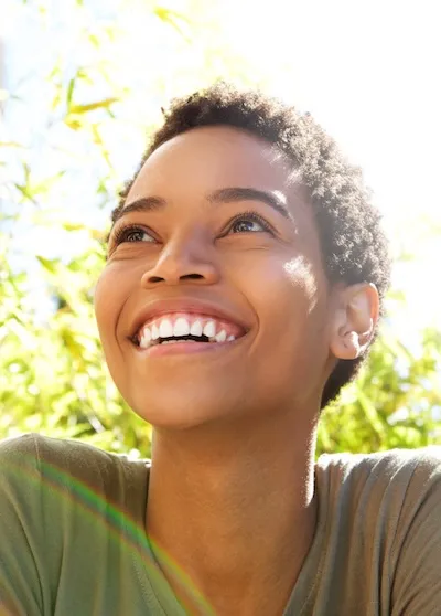 Kurs Buddhismus Gluecklich sein Ein Bild einer lachenden jungen Frau, den Blick in Richtung Himmel gerichtet.