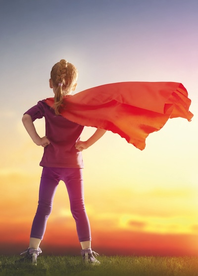Meditation-Kurs-Selbstvertrauen entwickeln Foto eines jungen Mädchens mit rotem Superman-atigen-Umhang, der im Wind weht. Arme auf den Hüften aufgestützt, Blick Richtung Sonne.
