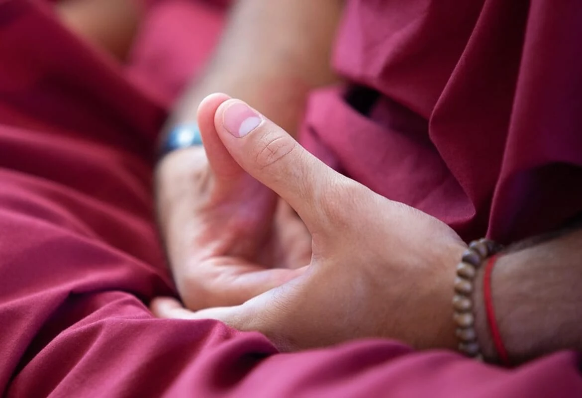 Eine Nahaufnahme von von zwei Händen in Meditationshaltung. Die Aussenseite der rechten Finger ruht auf der Innenseite der linken Hand. Die Daumen berühren sich.