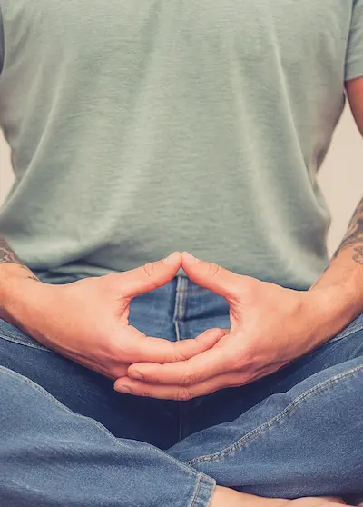kurs-tagesretreat-meditieren-lernen Bild eines Mannes in meditativer Sitzuhaltung mit überkreuzten Beinen. Hände ineinandergelegt im Schoss ruhend